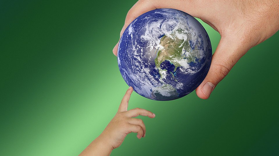 Erwachsenenhand hält Globus, Kinderhand tippt darauf.