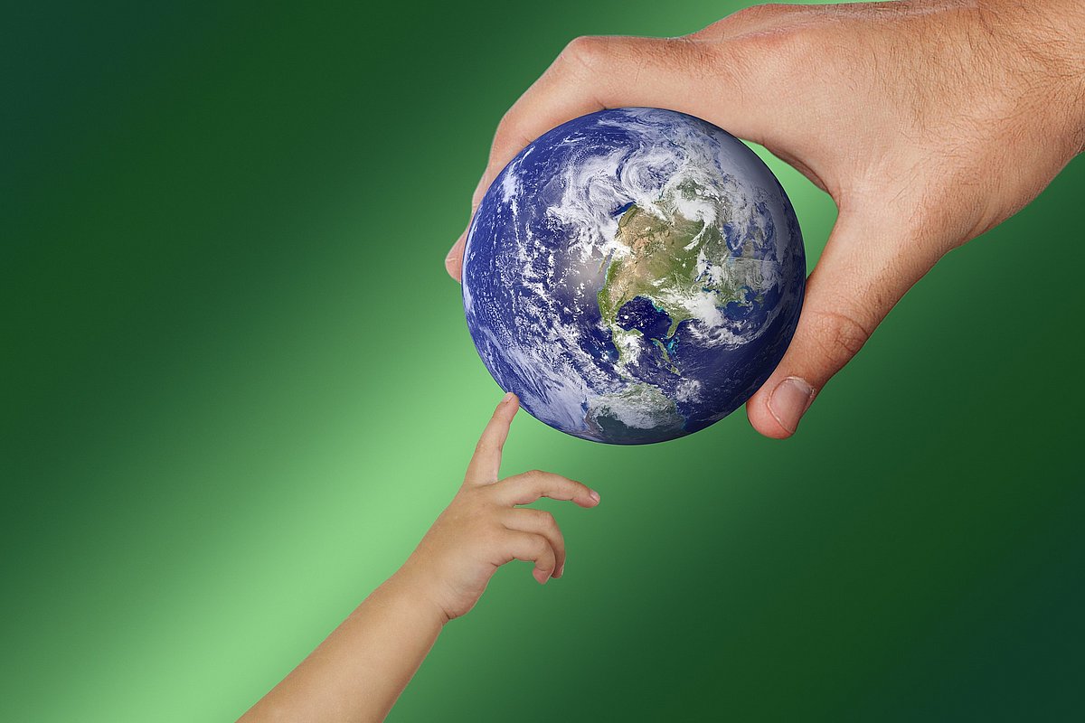 Erwachsenenhand hält Globus, Kinderhand tippt darauf.