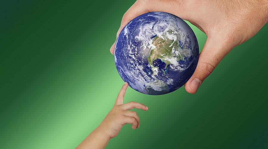 Erwachsenenhand hält Globus, Kinderhand tippt darauf.