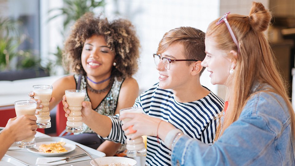 Teenager sitzen in Schulmensa am Tisch und unterhalten sich.