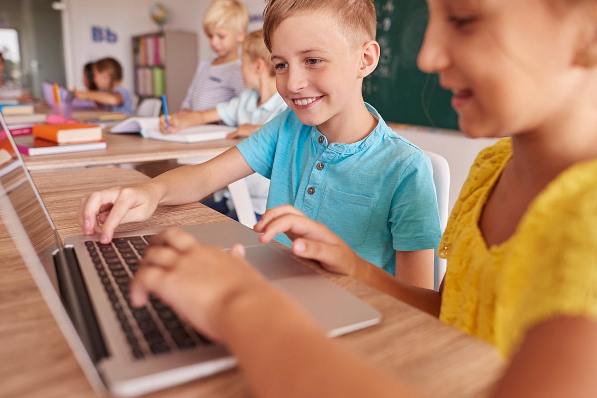 Zwei Schulkinder sitzen im Unterricht vor einem Laptop. 