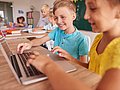 Zwei Schulkinder sitzen im Unterricht vor einem Laptop. 