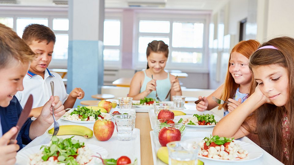 Teenager sitzen in einer Schulmensa am gedeckten Tisch.