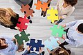 Menschen stehen im Kreis mit bunten Puzzel-Teilen in der Hand