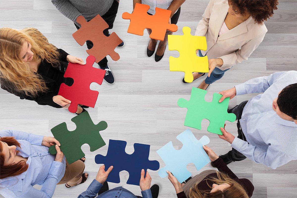 Menschen stehen im Kreis mit bunten Puzzel-Teilen in der Hand