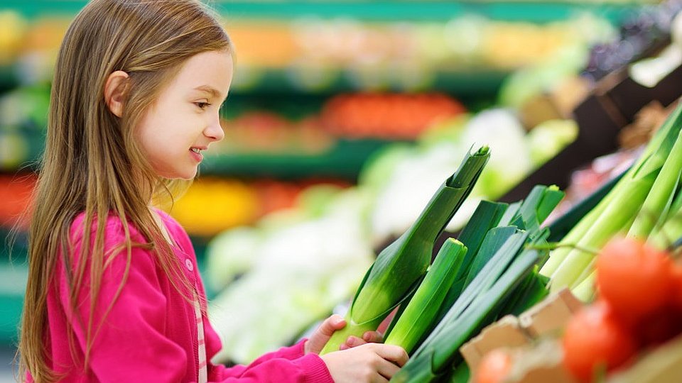 Ein Schulkind kauft Gemüse in einem Supermarkt.