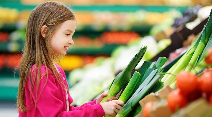 Ein Schulkind kauft Gemüse in einem Supermarkt.
