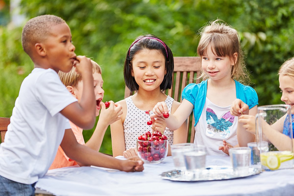 Kinder, die zusammen an einem Tisch sitzen und Kirschen essen.