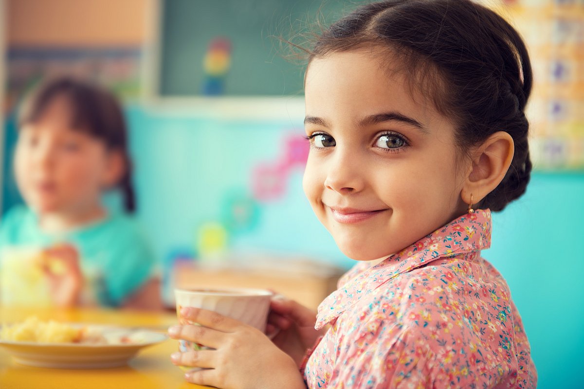 Mädchen in der Kita hält einen Becher und lächelt in die Kamera