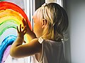 Kita-Kind malt mit Fingerfarben einen Regenbogen ans Fenster. 