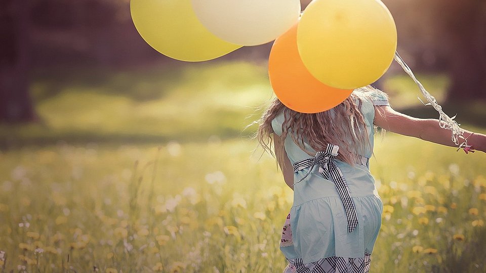 Ein glücklichen Mädchen rennt über eine Wiese mit bunten Luftballons