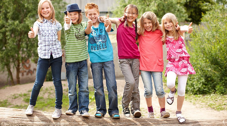 Eine Gruppe Grundschulkinder turnt auf einem Baumstamm. 