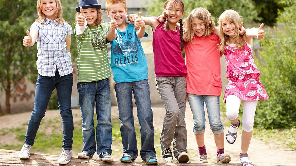 Eine Gruppe Grundschulkinder turnt auf einem Baumstamm. 