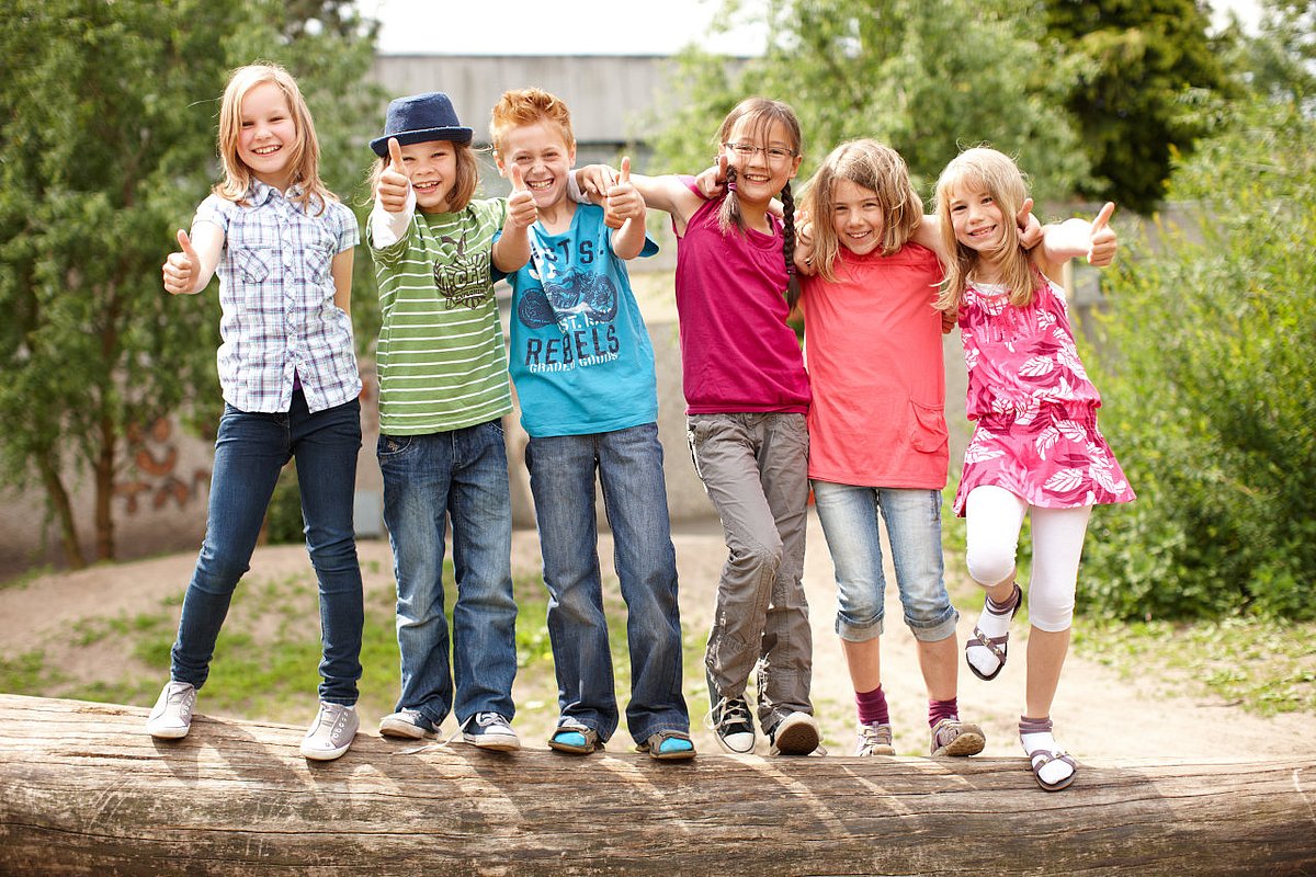 Eine Gruppe Grundschulkinder turnt auf einem Baumstamm. 