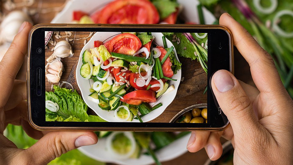 Hände fotografieren Salat mit Mobiltelefon.