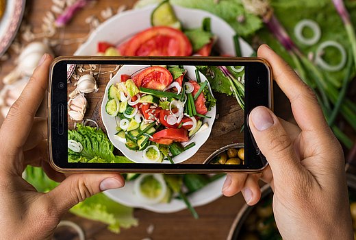 Hände fotografieren Salat mit Mobiltelefon.