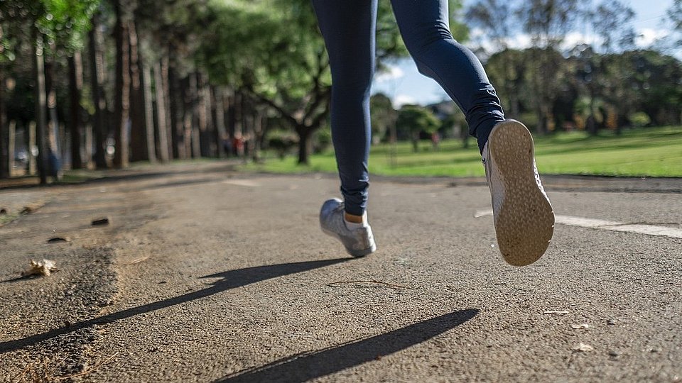 Ein Mensch, von dem nur die Beine zu sehen sind, joggt über einen Weg.