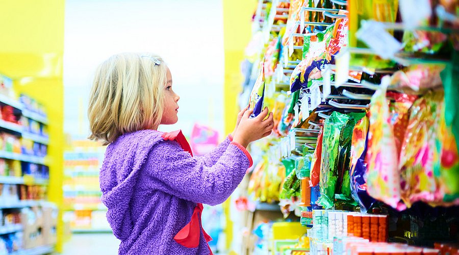Ein Mädchen steht vor einer Wand mit Süßigkeiten in einem Supermarkt. 