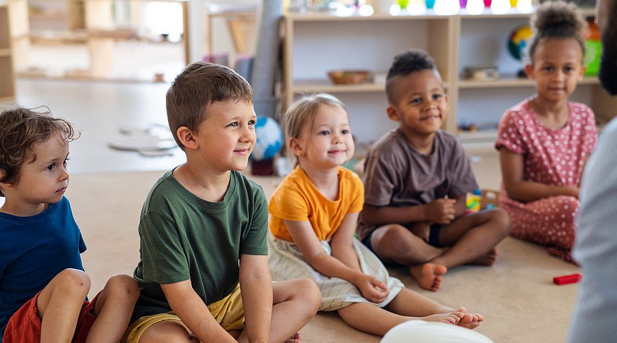 Kita-Kinder sitzen im Halbkreis und hören einer Geschichte zu.  