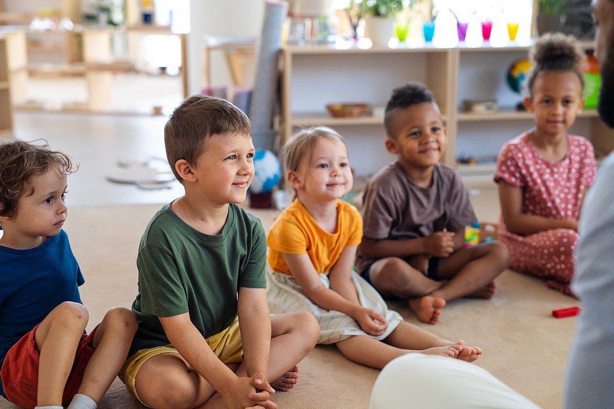 Kita-Kinder sitzen im Halbkreis und hören einer Geschichte zu.  