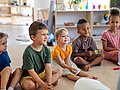 Kita-Kinder sitzen im Halbkreis und hören einer Geschichte zu.  