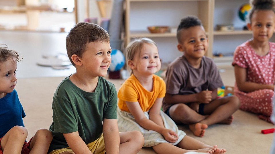Kita-Kinder sitzen im Halbkreis und hören einer Geschichte zu.  