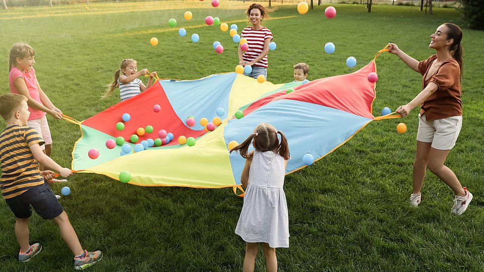 Grundschulkinder spielen mit Lehrkräften auf dem Rasen ein Spiel. 