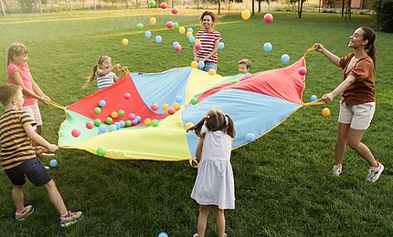 Grundschulkinder spielen mit Lehrkräften auf dem Rasen ein Spiel. 