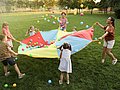 Grundschulkinder spielen mit Lehrkräften auf dem Rasen ein Spiel. 