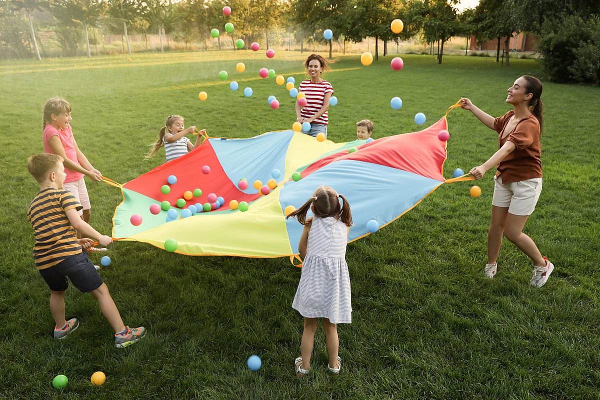 Grundschulkinder spielen mit Lehrkräften auf dem Rasen ein Spiel. 