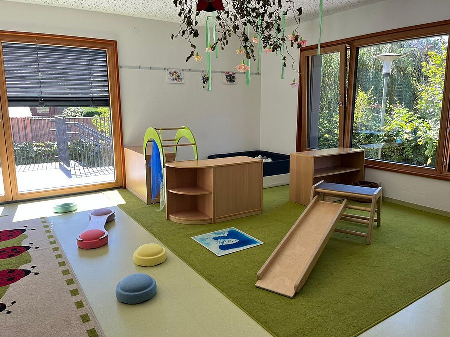 Kita-Raum Innenansicht: Große Fenster zum Garten und Spielgeräte innen.