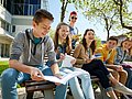 Jugendliche Schüler*innen sitzen mit ihren Schulunterlagen gemeinsam auf einer Bank. 
