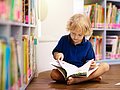 Kind liest vor einem Bücherregal in einem Buch.