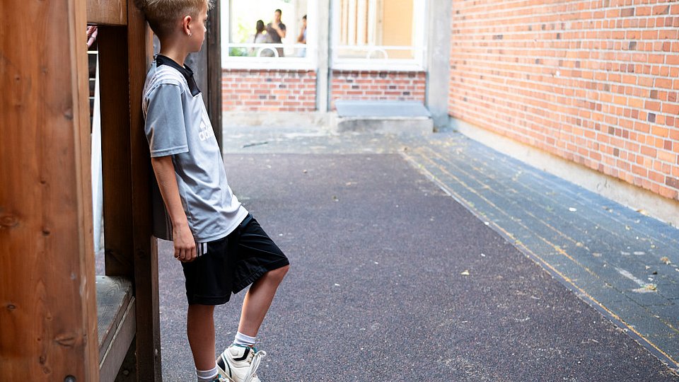 Ein Junge steht auf dem Spielplatz der Grundschule.  