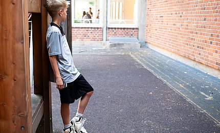 Ein Junge steht auf dem Spielplatz der Grundschule.  