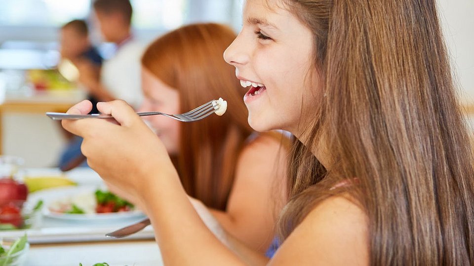 Jugendliche Schülerin sitzt in der Mensa und isst.