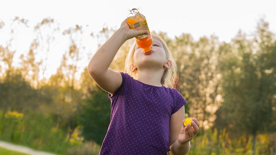 Schulkind trinkt Limonade aus einer Plastikflasche. 