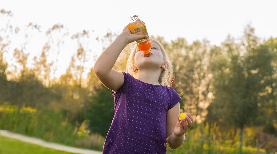 Schulkind trinkt Limonade aus einer Plastikflasche. 