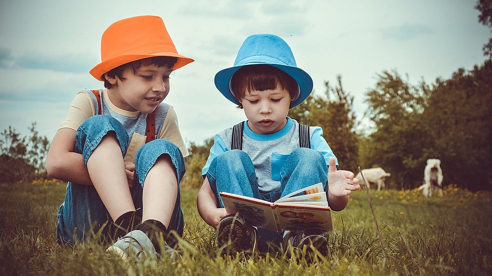 zwei lesende Kinder auf einer Wiese