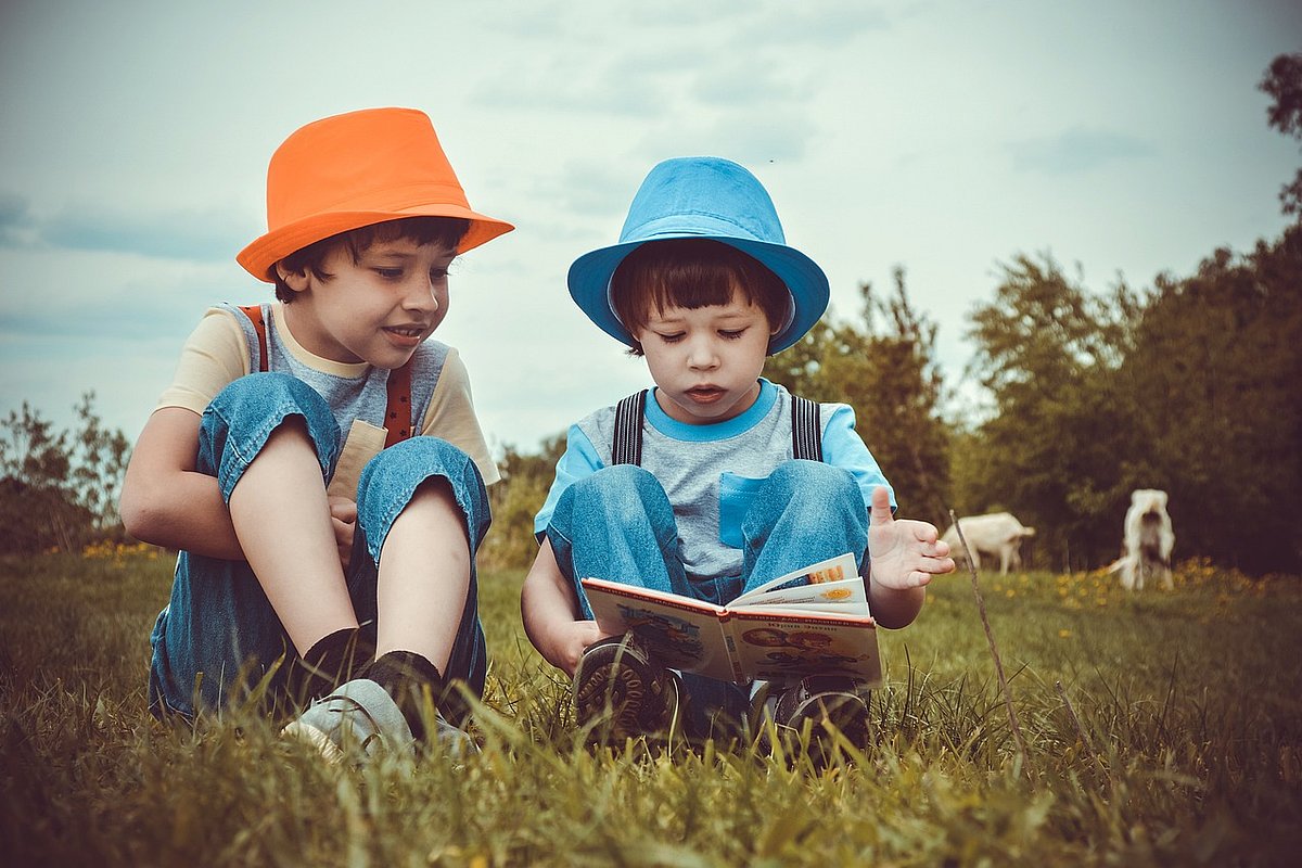 zwei lesende Kinder auf einer Wiese