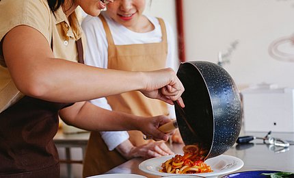 Jugendliche Schülerinnen bereiten sich Spaghetti mit Tomatensauce zu. 