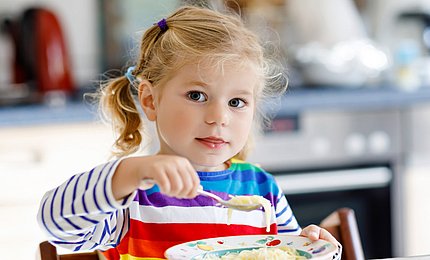 Kleinkind sitzt am Tisch und isst.