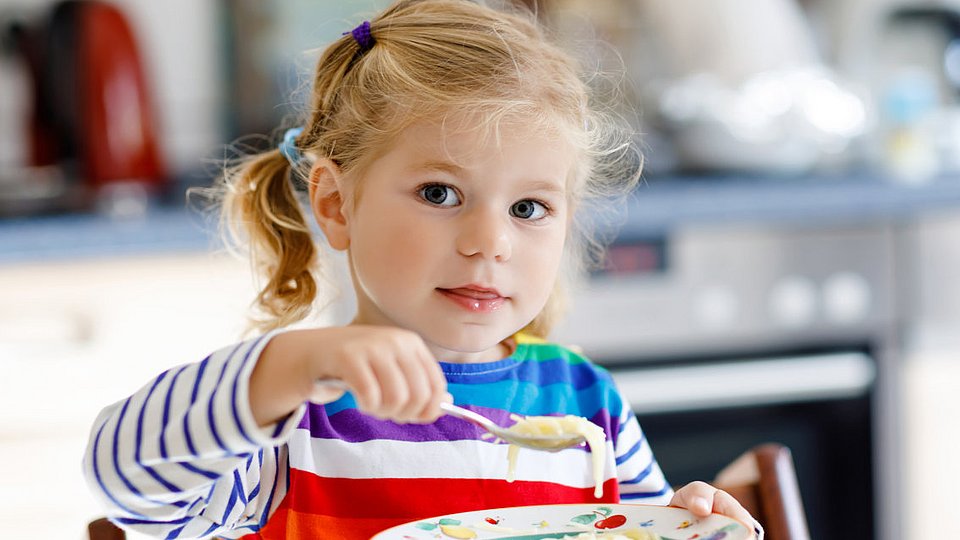 Kleinkind sitzt am Tisch und isst.