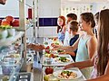 Kinder stehen in einer Schulmensa an der Ausgabetheke und suchen sich ihr Essen aus.