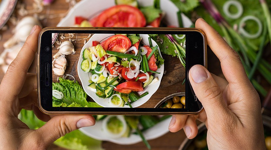 Hände fotografieren Salat mit Mobiltelefon.