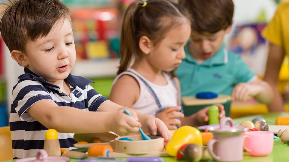 Kita-Kinder spielen mit Geschirr und Lebensmitteln aus Holz.