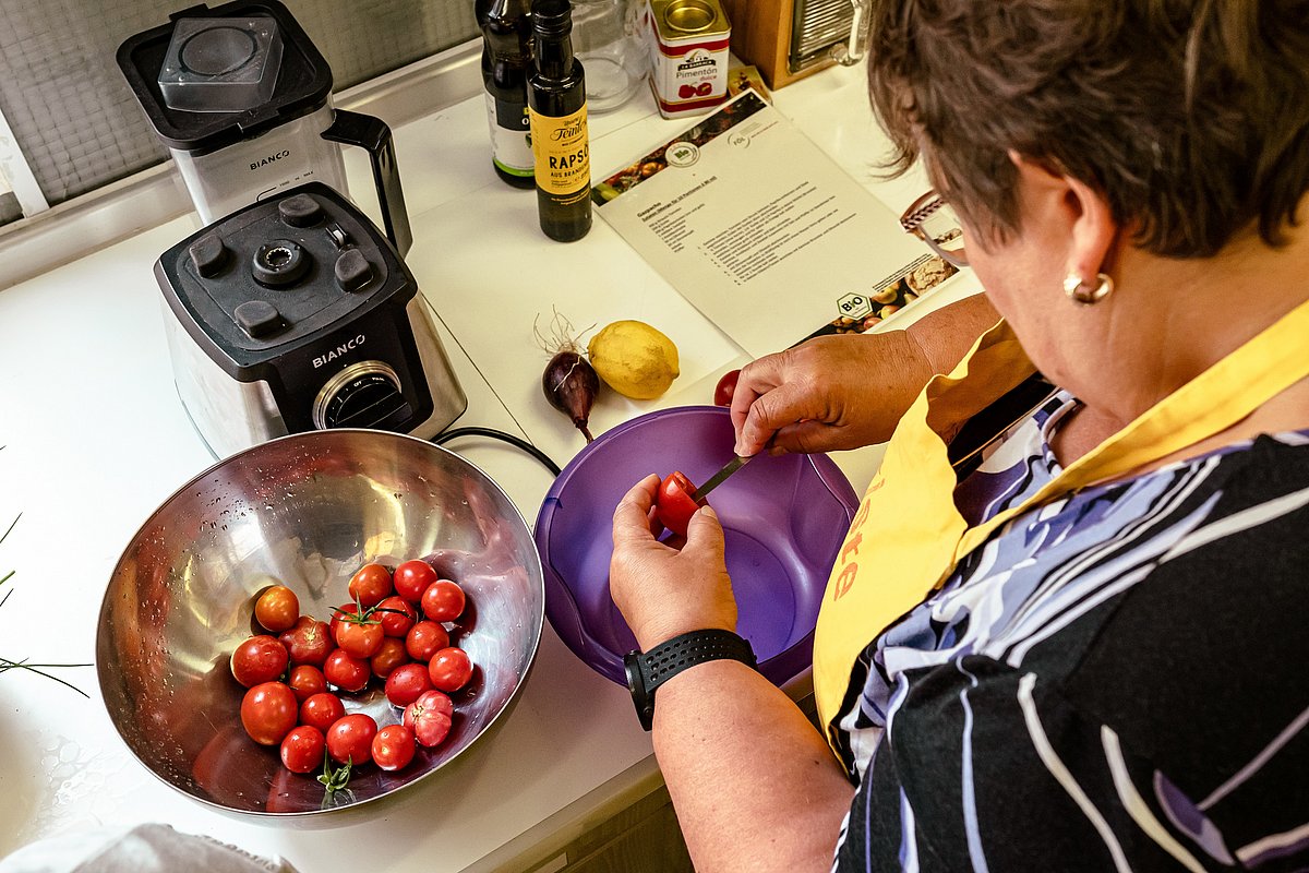 Eine Frau steht in einer Küche, mit Schürze, und putzt Obst.