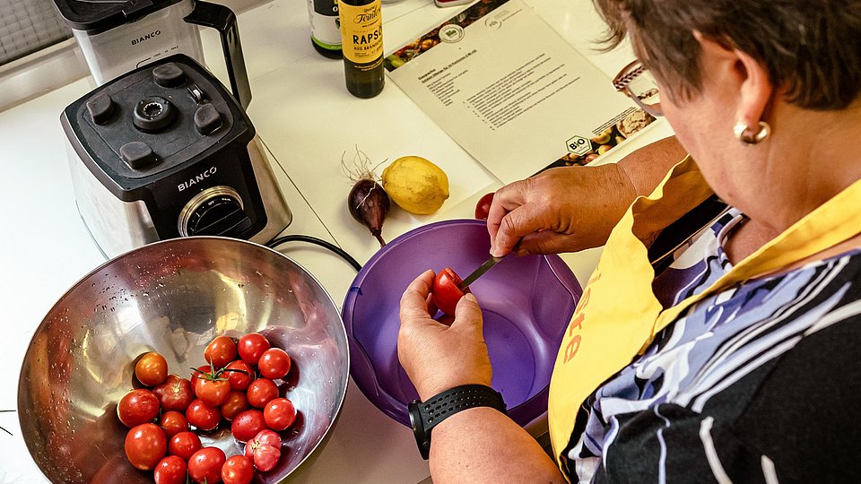 Eine Frau steht in einer Küche, mit Schürze, und putzt Obst.