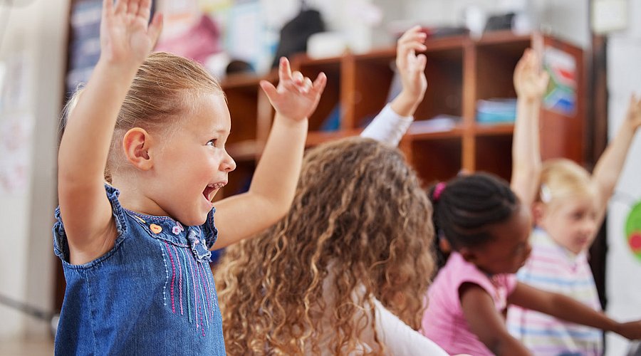 Kita-Kinder sitzen im Kreis und spielen ein Bewegungsspiel. 
