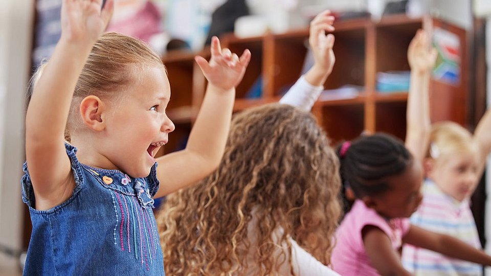 Kita-Kinder sitzen im Kreis und spielen ein Bewegungsspiel. 